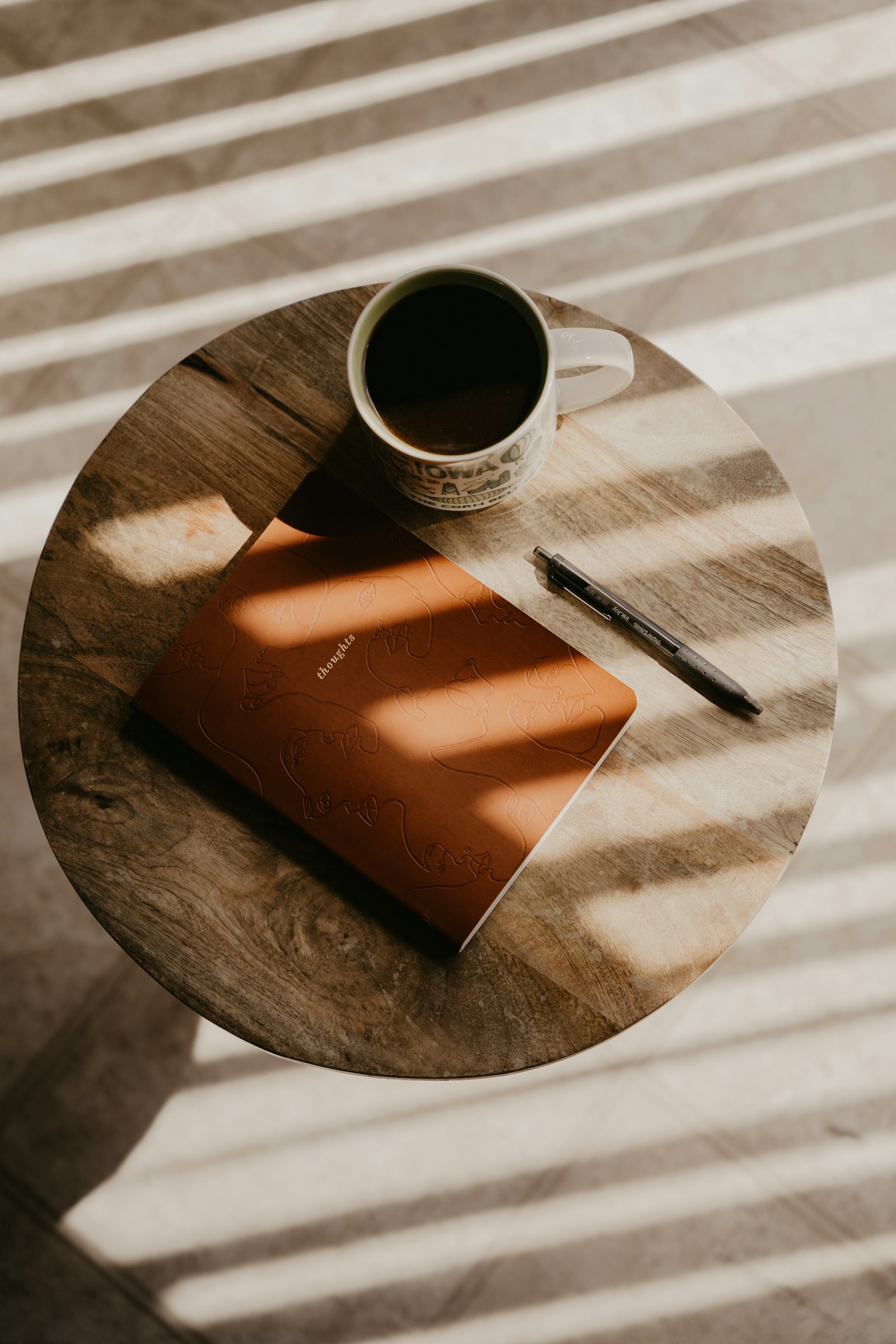 A leather notebook, pen and coffee on a wooden table in dramatic morning light